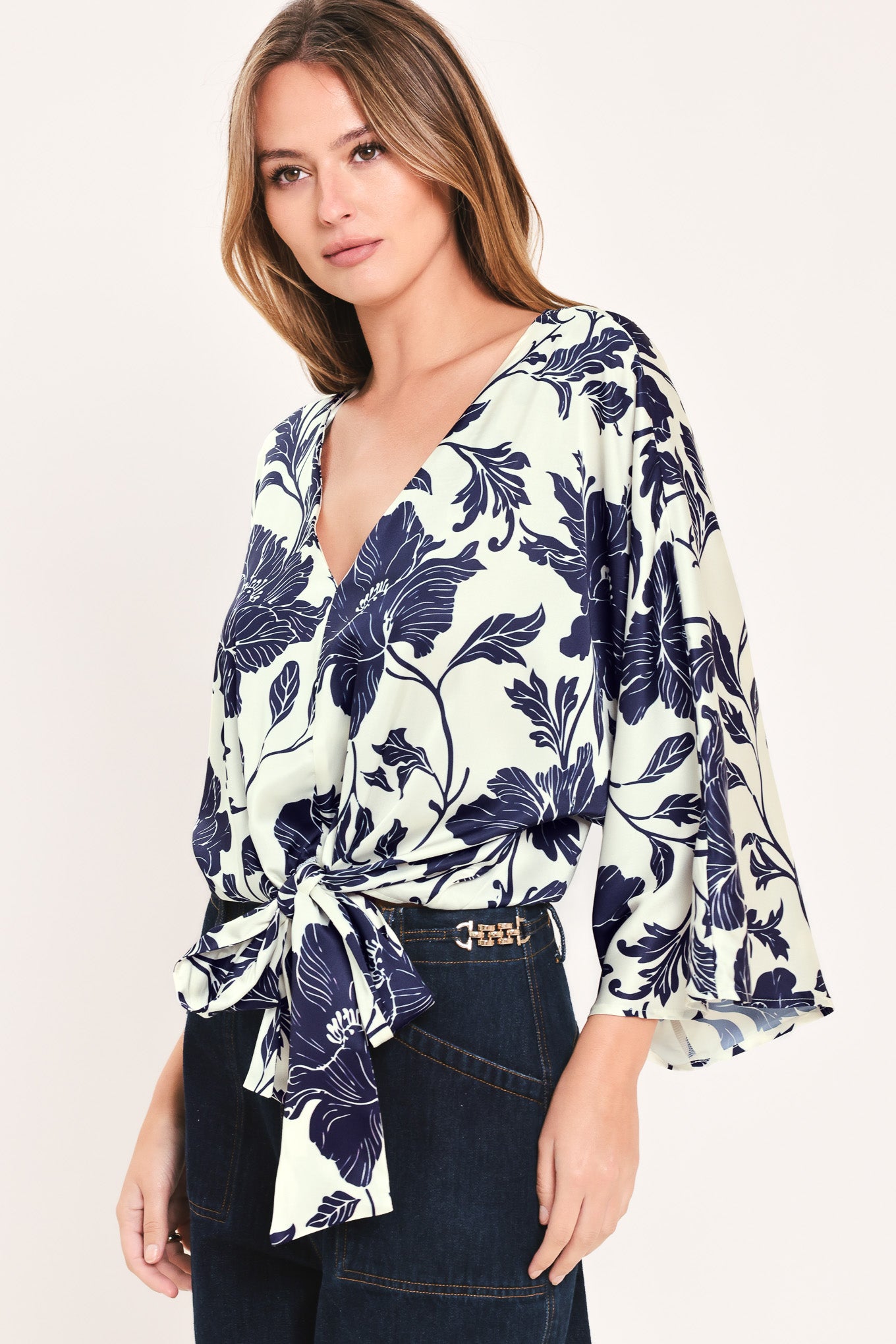 A woman wearing a navy blue and off-white floral print wrap top with wide bell sleeves and a tie waist | Flying Tomato