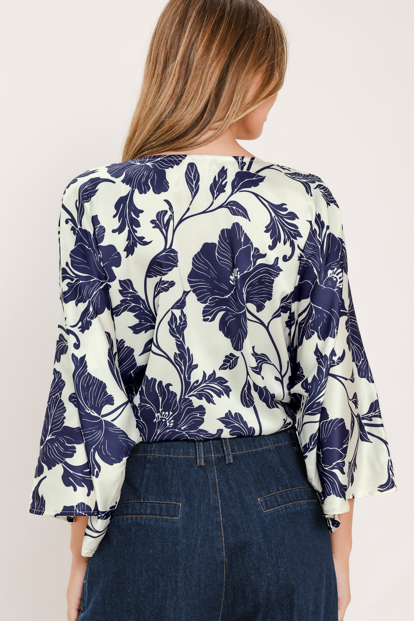 A woman wearing a navy blue and off-white floral print wrap top with wide bell sleeves and a tie waist | Flying Tomato