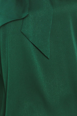 A woman wearing a dark hunter green satin blouse with a high neck, large bow at the collar, and gathered long sleeves with gold button accents | Flying Tomato