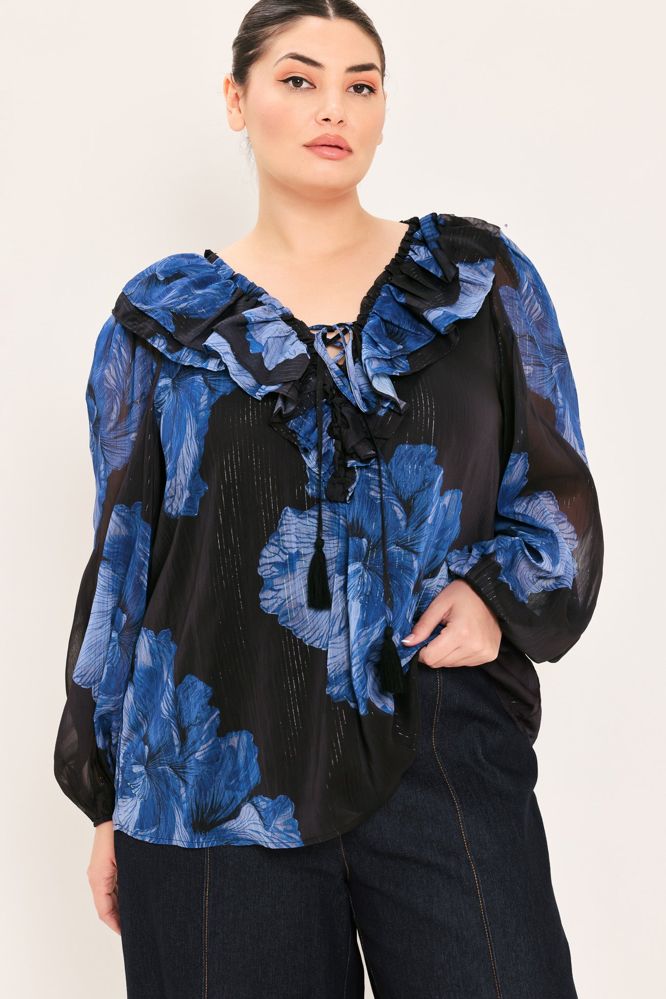 A woman wearing a black blouse with a blue floral print and ruffled collar details | Plus Curve Flying Tomato