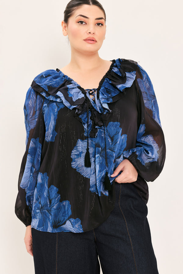 A woman wearing a black blouse with a blue floral print and ruffled collar details | Plus Curve Flying Tomato