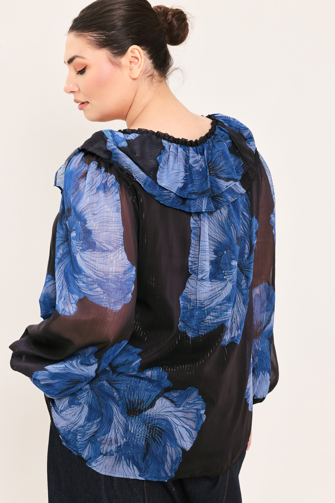 A woman wearing a black blouse with a blue floral print and ruffled collar details | Plus Curve Flying Tomato