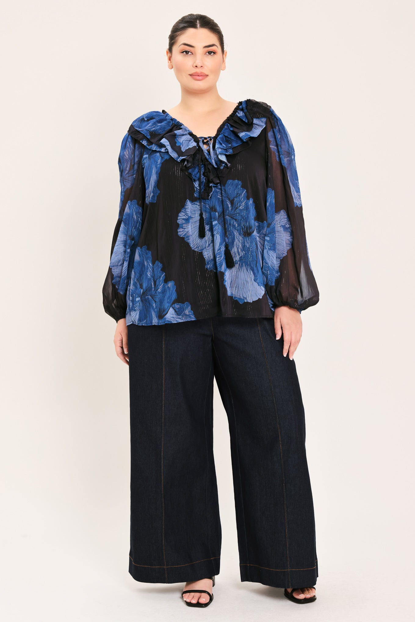 A woman wearing a black blouse with a blue floral print and ruffled collar details | Plus Curve Flying Tomato
