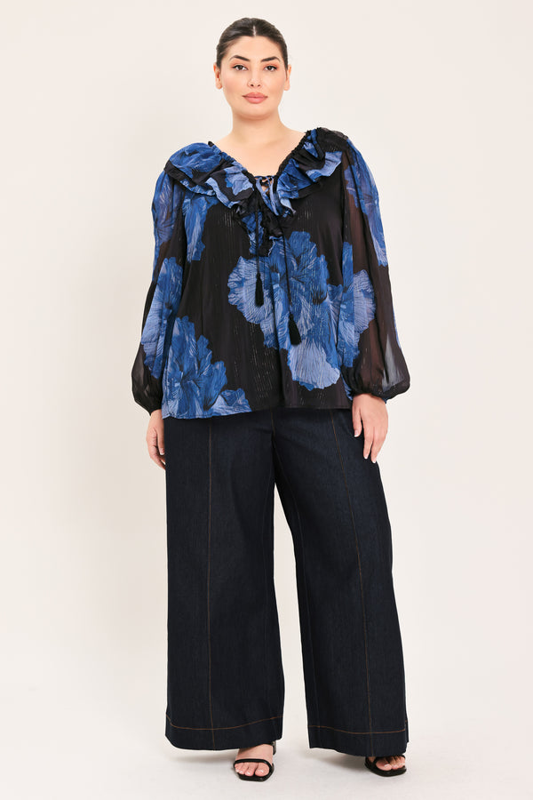 A woman wearing a black blouse with a blue floral print and ruffled collar details | Plus Curve Flying Tomato