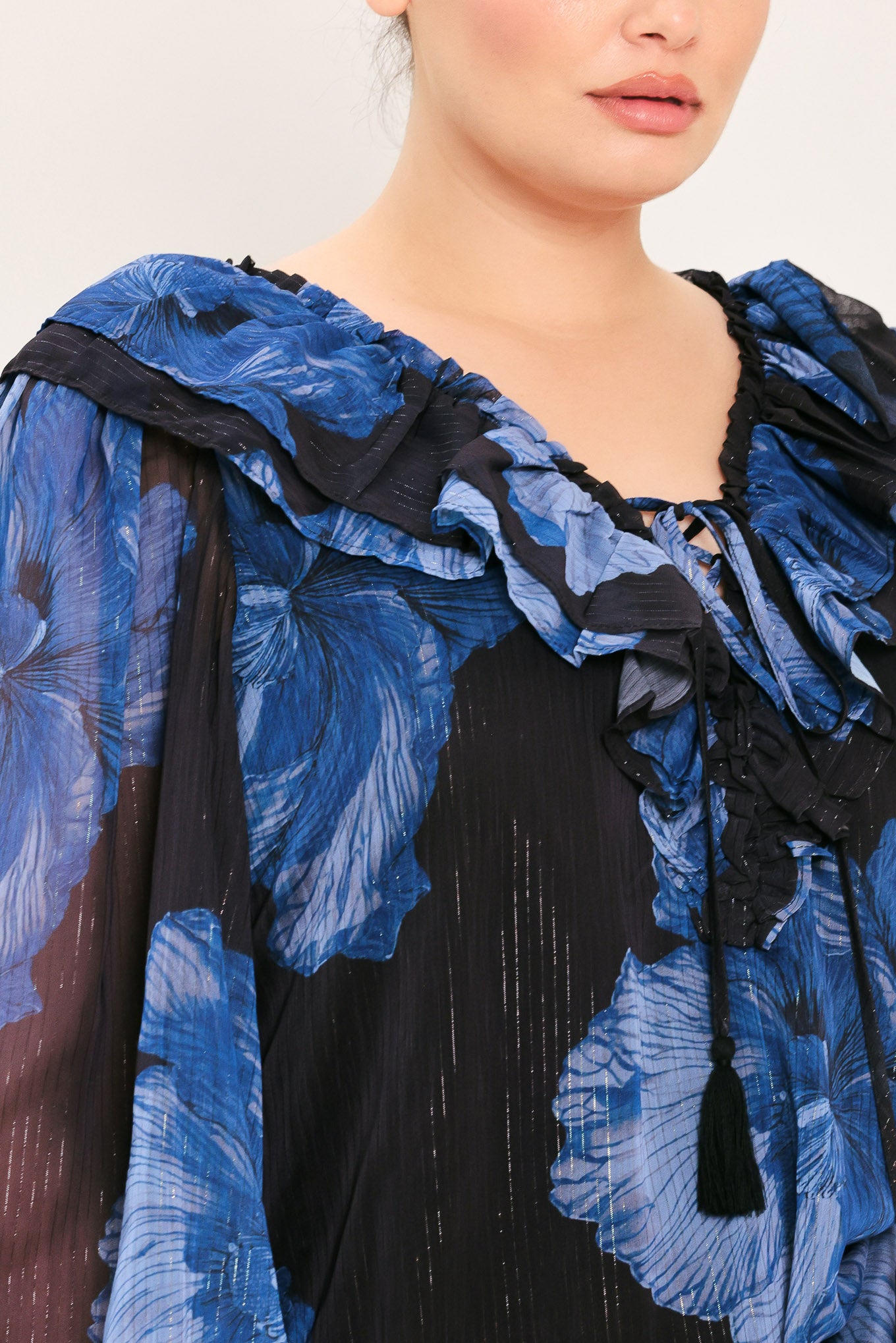 A woman wearing a black blouse with a blue floral print and ruffled collar details | Plus Curve Flying Tomato