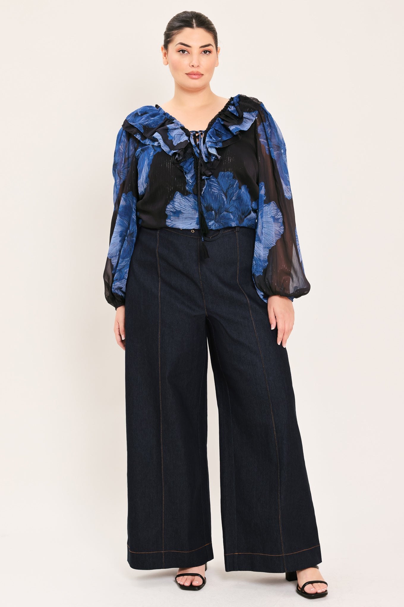 A woman wearing a black blouse with a blue floral print and ruffled collar details | Plus Curve Flying Tomato