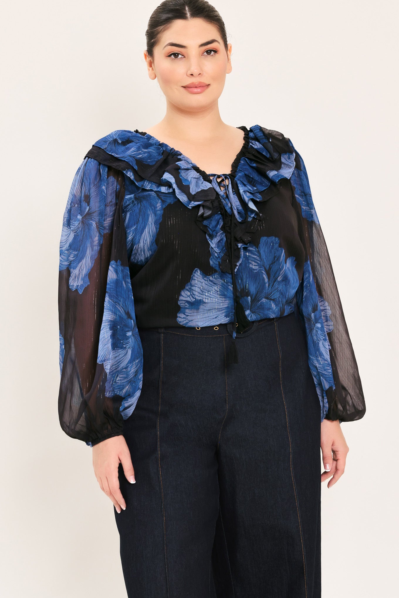 A woman wearing a black blouse with a blue floral print and ruffled collar details | Plus Curve Flying Tomato