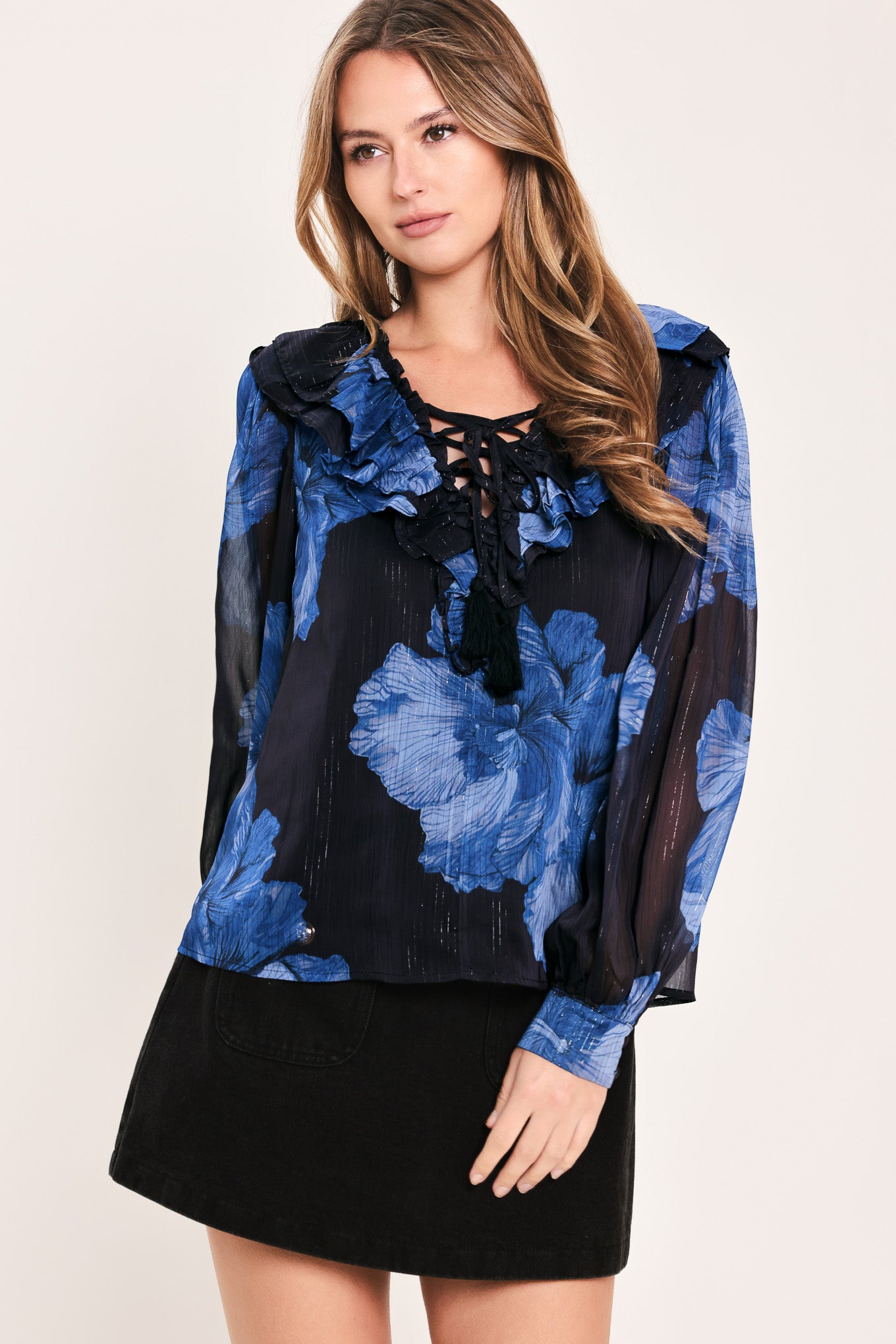 A woman wearing a sheer black blouse with a blue floral print, ruffled collar, and lace-up neckline | Flying Tomato