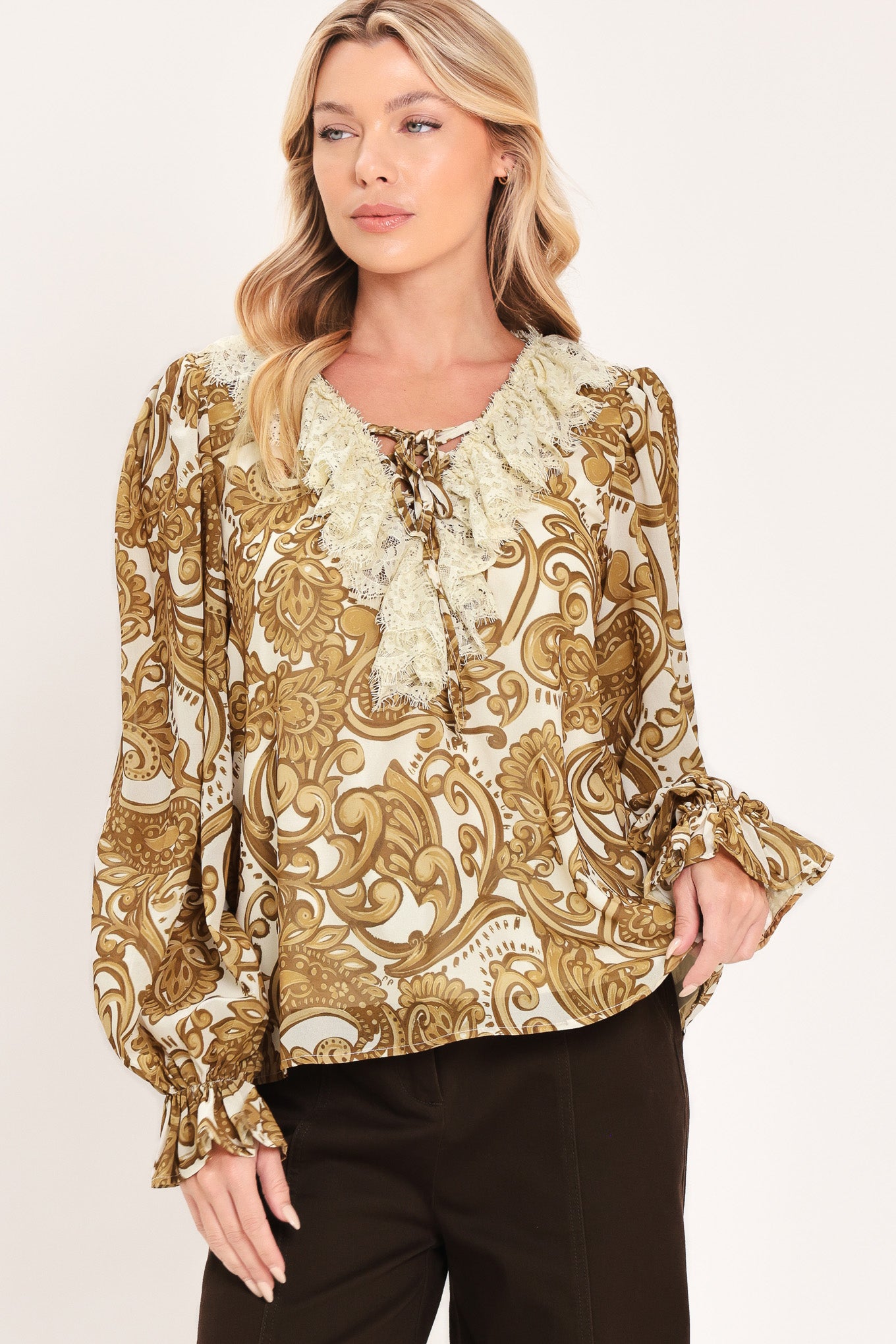 A woman wearing a long-sleeve blouse with a gold and beige baroque-style pattern, a ruffled lace-up neckline, and ruffled cuffs | Flying Tomato