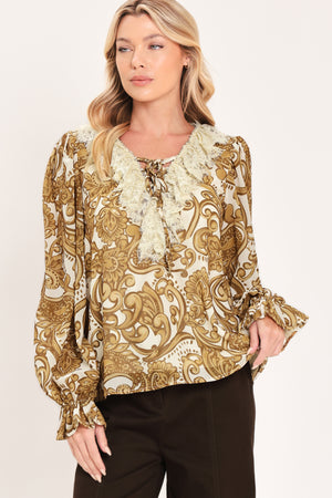 A woman wearing a long-sleeve blouse with a gold and beige baroque-style pattern, a ruffled lace-up neckline, and ruffled cuffs | Flying Tomato