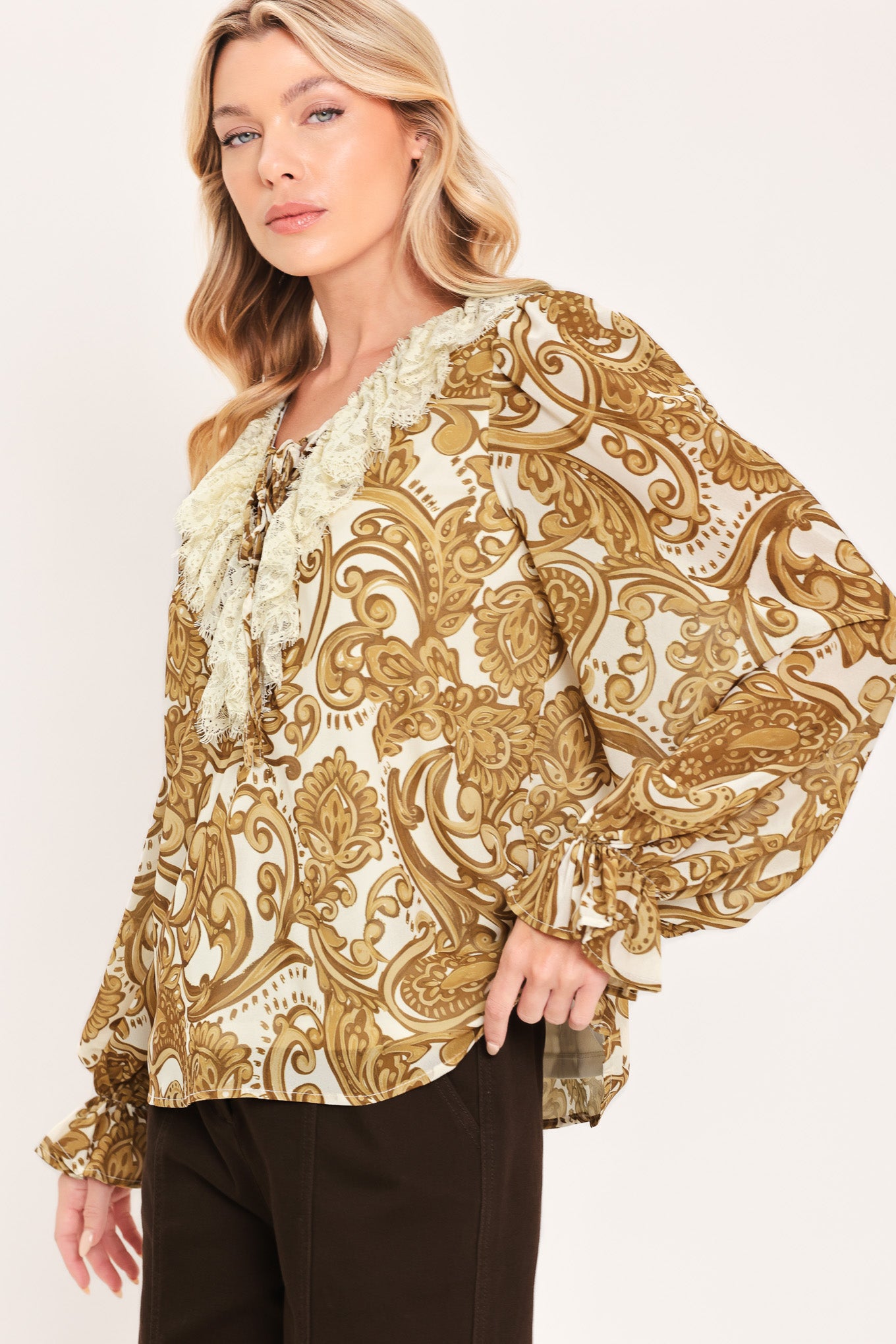 A woman wearing a long-sleeve blouse with a gold and beige baroque-style pattern, a ruffled lace-up neckline, and ruffled cuffs | Flying Tomato