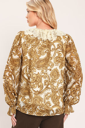 A woman wearing a long-sleeve blouse with a gold and beige baroque-style pattern, a ruffled lace-up neckline, and ruffled cuffs | Flying Tomato