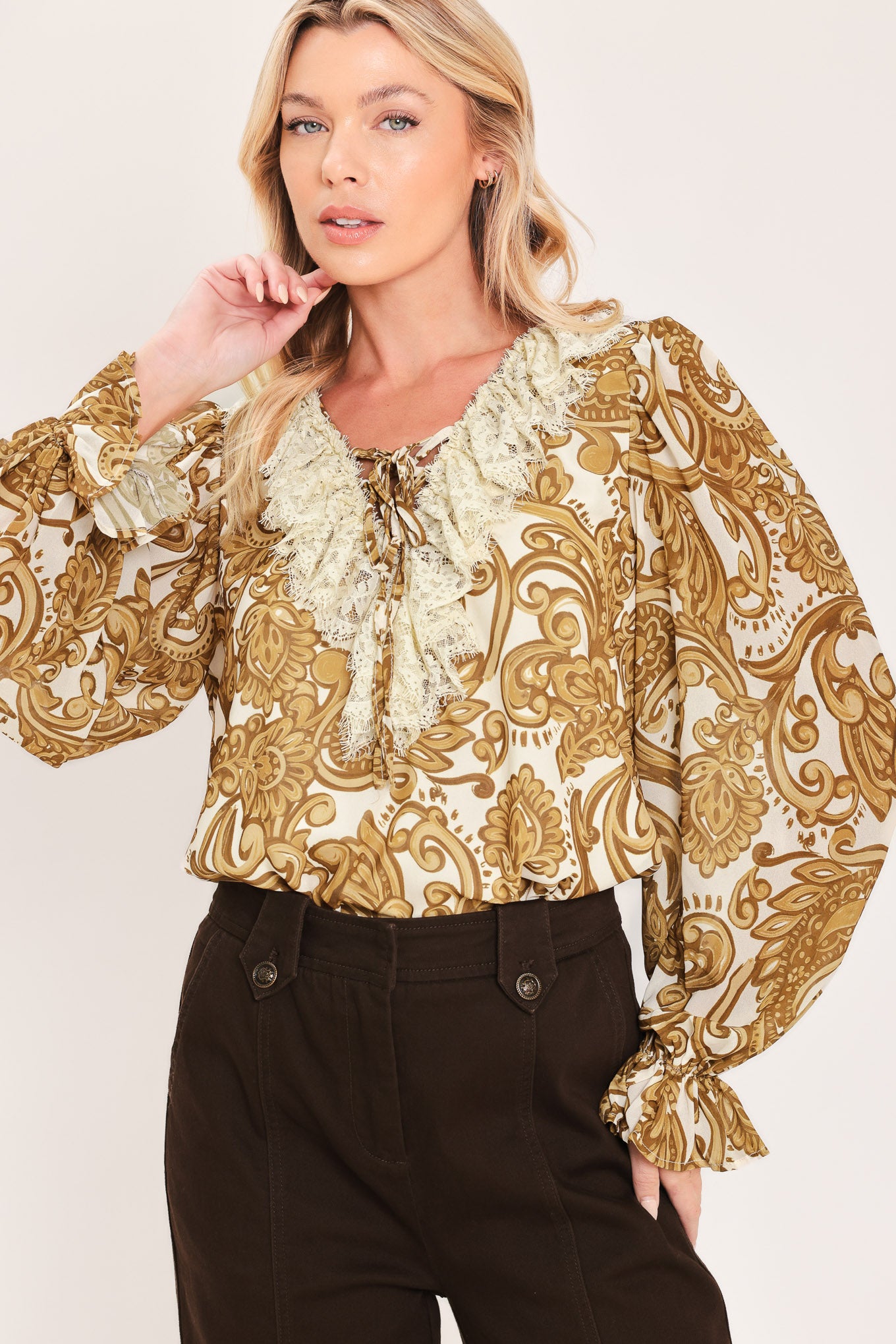 A woman wearing a long-sleeve blouse with a gold and beige baroque-style pattern, a ruffled lace-up neckline, and ruffled cuffs | Flying Tomato
