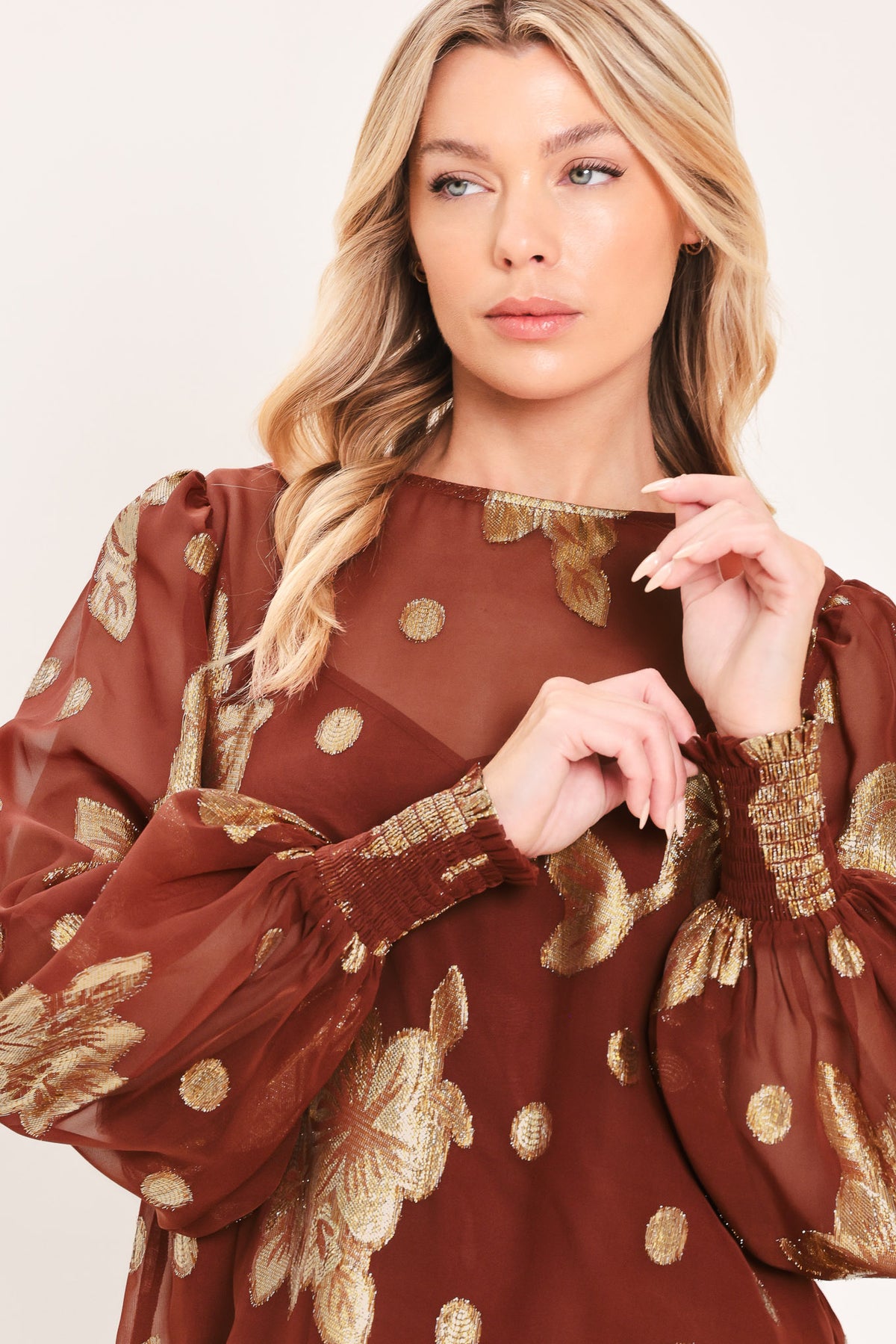 A woman wearing a sheer rust-brown/brick-colored blouse with metallic gold floral embroidery and puff sleeves | Flying Tomato