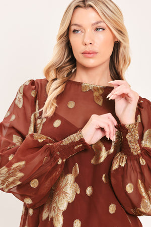A woman wearing a sheer rust-brown/brick-colored blouse with metallic gold floral embroidery and puff sleeves | Flying Tomato