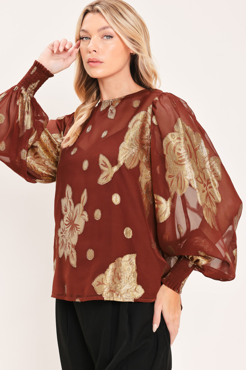 A woman wearing a sheer rust-brown/brick-colored blouse with metallic gold floral embroidery and puff sleeves | Flying Tomato