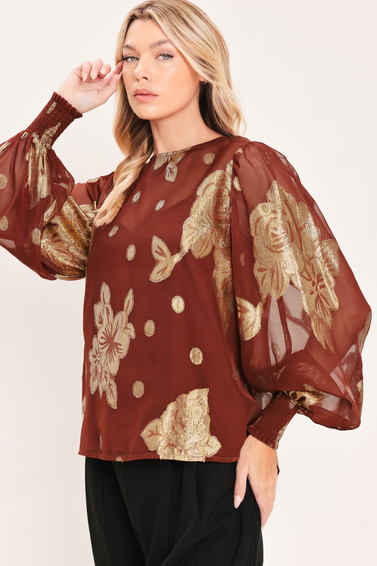 A woman wearing a sheer rust-brown/brick-colored blouse with metallic gold floral embroidery and puff sleeves | Flying Tomato