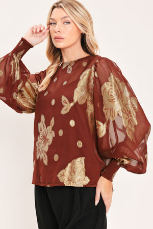 A woman wearing a sheer rust-brown/brick-colored blouse with metallic gold floral embroidery and puff sleeves | Flying Tomato