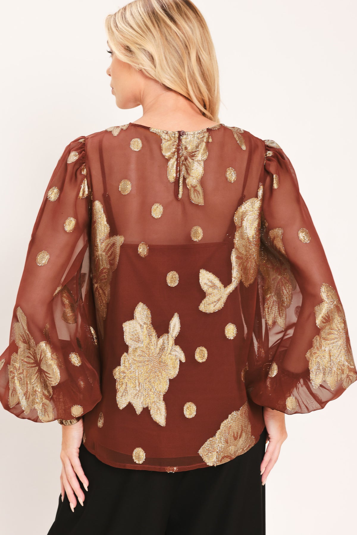 A woman wearing a sheer rust-brown/brick-colored blouse with metallic gold floral embroidery and puff sleeves | Flying Tomato