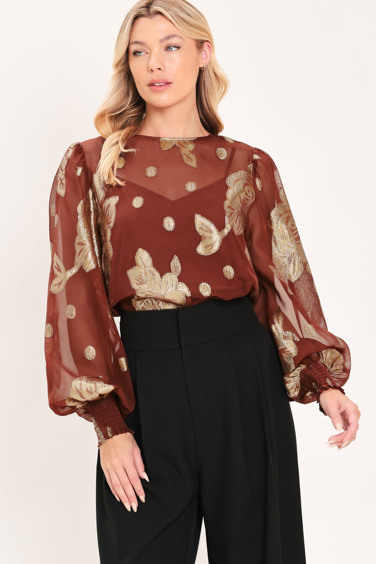 A woman wearing a sheer rust-brown/brick-colored blouse with metallic gold floral embroidery and puff sleeves | Flying Tomato