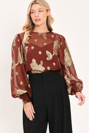 A woman wearing a sheer rust-brown/brick-colored blouse with metallic gold floral embroidery and puff sleeves | Flying Tomato