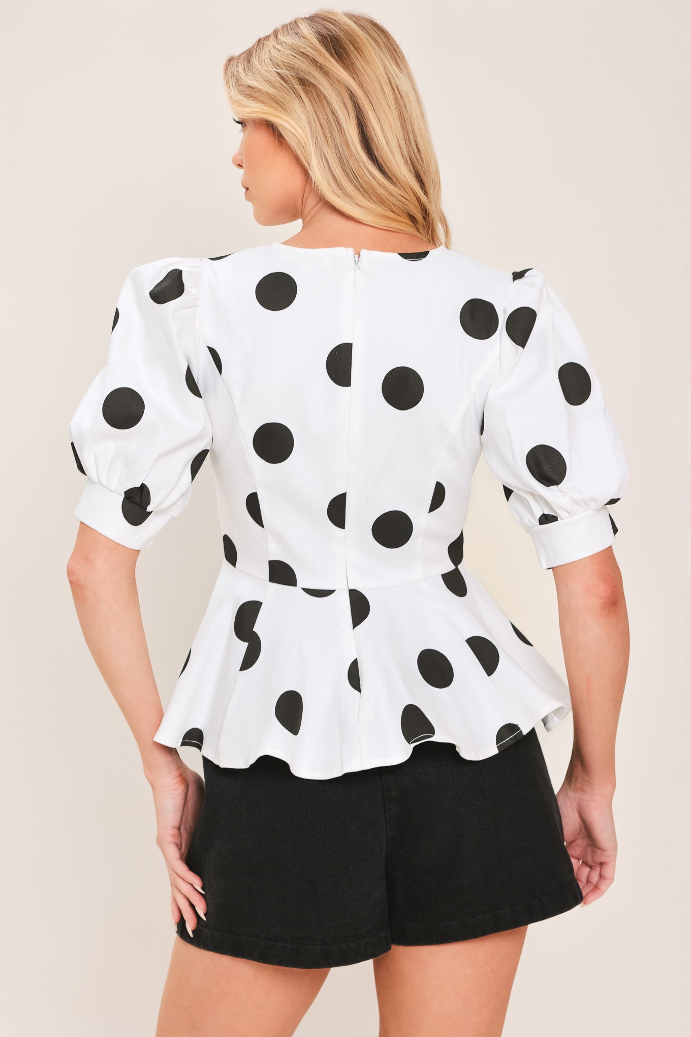 A woman wearing a white short-sleeve blouse with large black polka dots and puffed sleeves | Flying Tomato