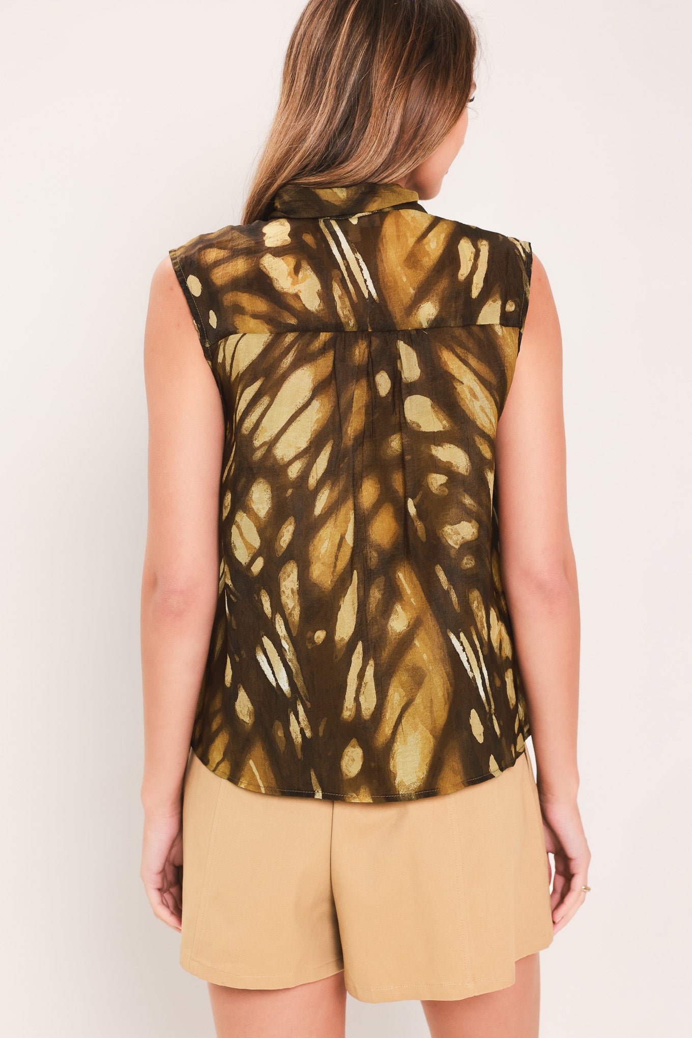 Woman wearing a dark brown sleeveless flowy top with a butterfly-like print and self tie bow around the neck | Flying Tomato