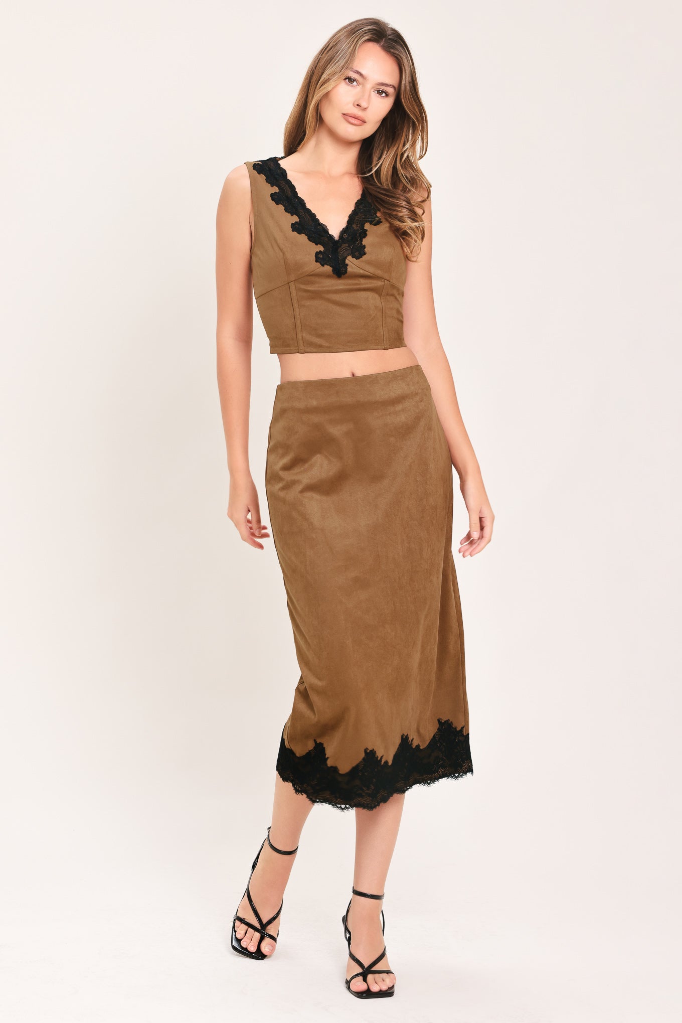 A woman wearing a faux suede brown sleeveless crop top with a black lace V-neck trim | Flying Tomato