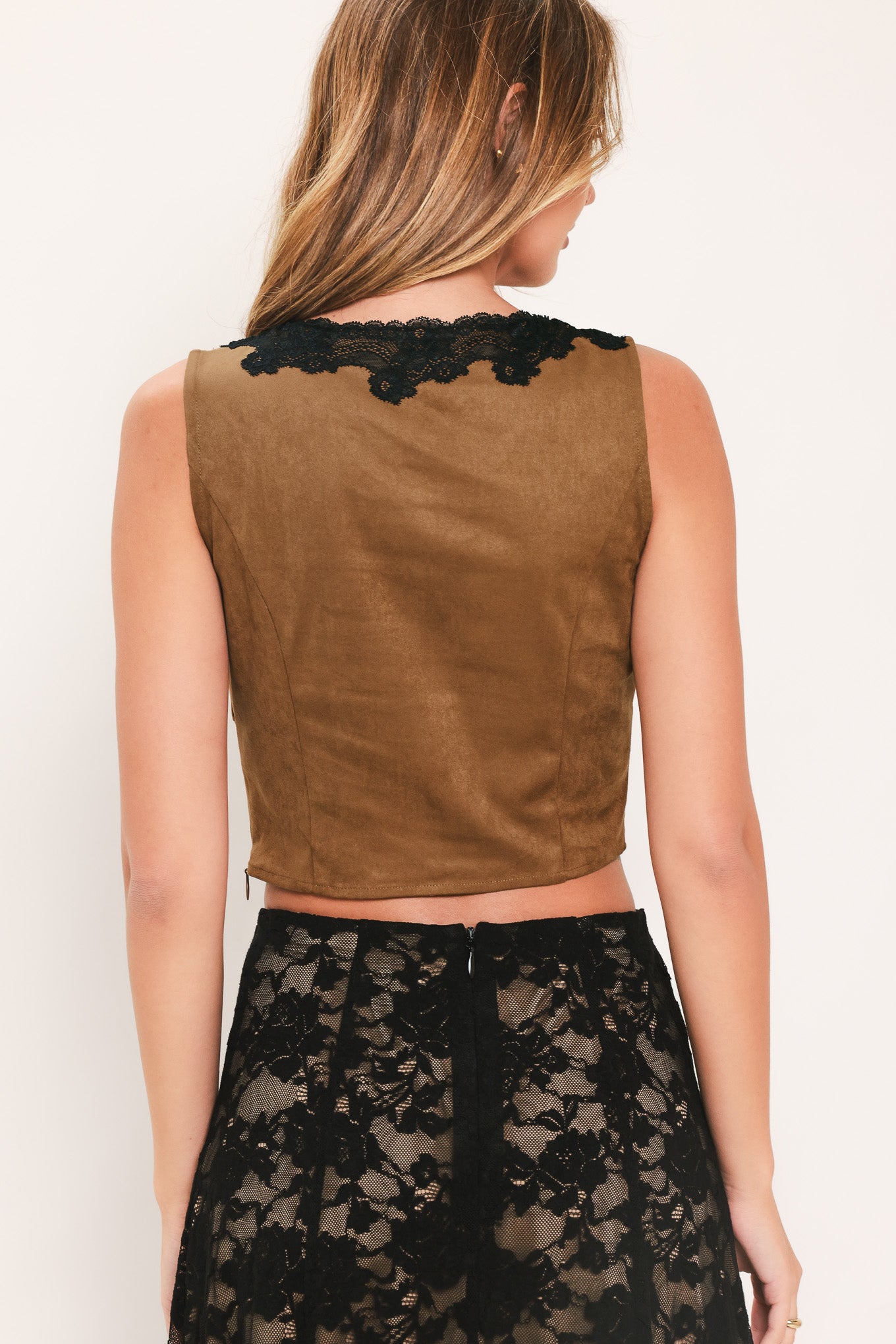 A woman wearing a faux suede brown sleeveless crop top with a black lace V-neck trim | Flying Tomato