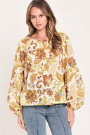 A woman wearing a long-sleeve blouse with a cream base and a brown and gold floral pattern | Flying Tomato