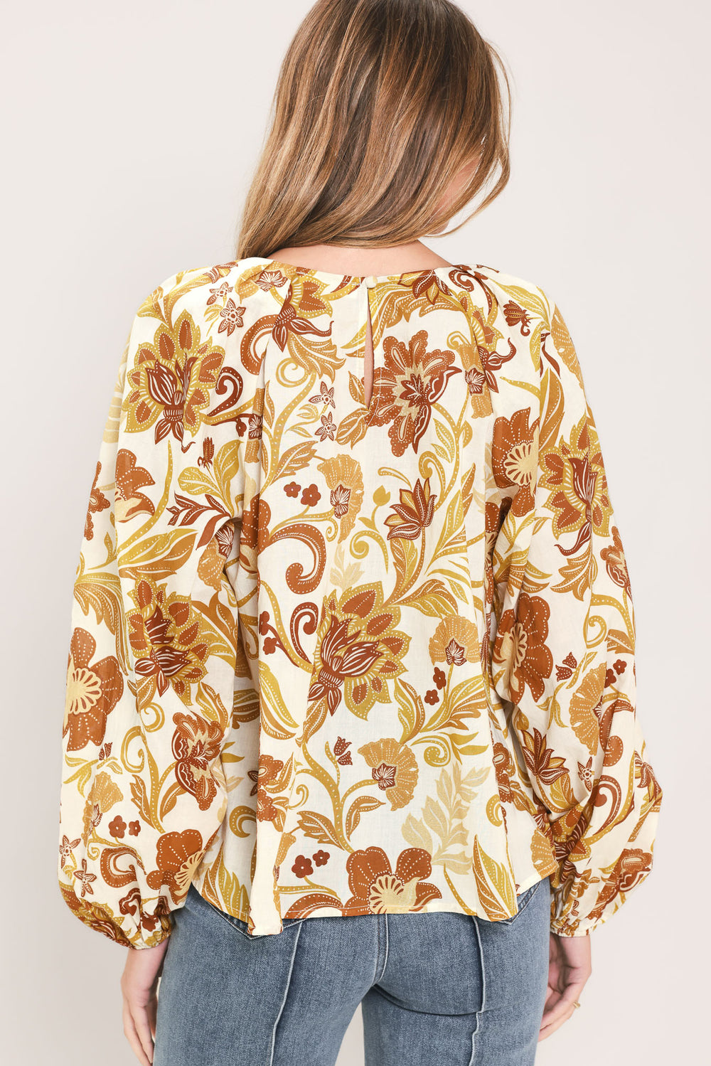 A woman wearing a long-sleeve blouse with a cream base and a brown and gold floral pattern | Flying Tomato