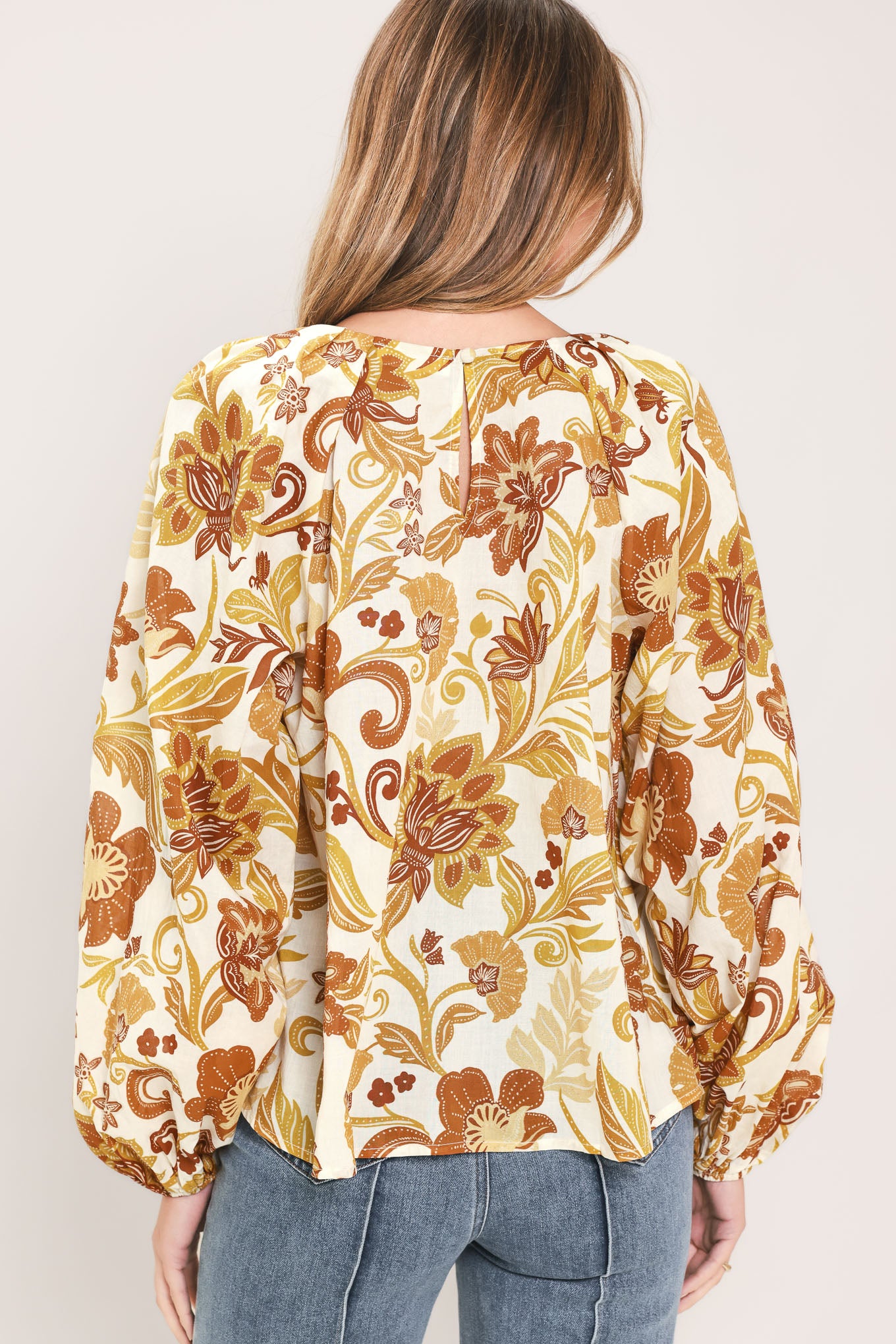 A woman wearing a long-sleeve blouse with a cream base and a brown and gold floral pattern | Flying Tomato