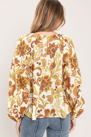 A woman wearing a long-sleeve blouse with a cream base and a brown and gold floral pattern | Flying Tomato