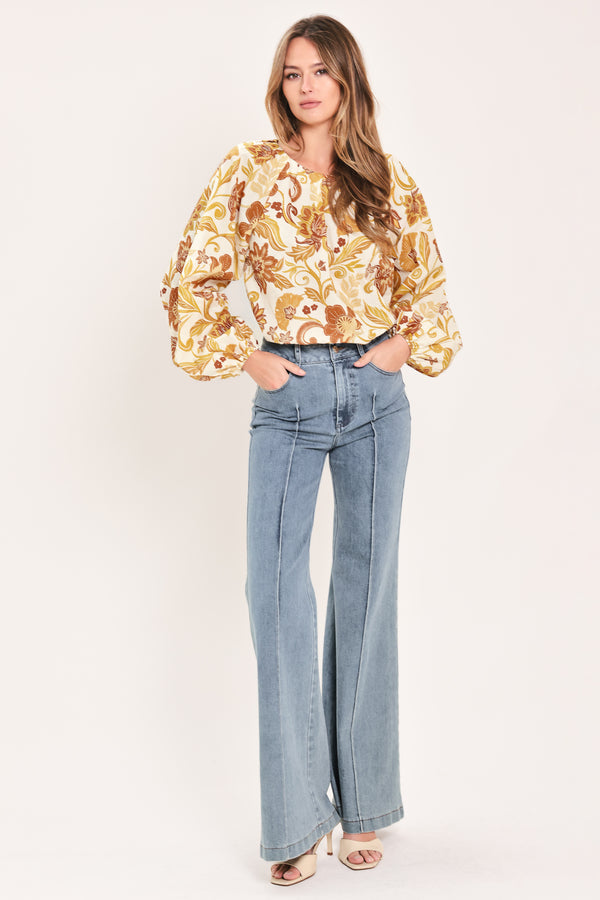 A woman wearing a long-sleeve blouse with a cream base and a brown and gold floral pattern | Flying Tomato