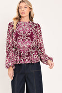 A woman modeling a long-sleeve peplum blouse with a burgundy and beige baroque-style pattern | Flying Tomato