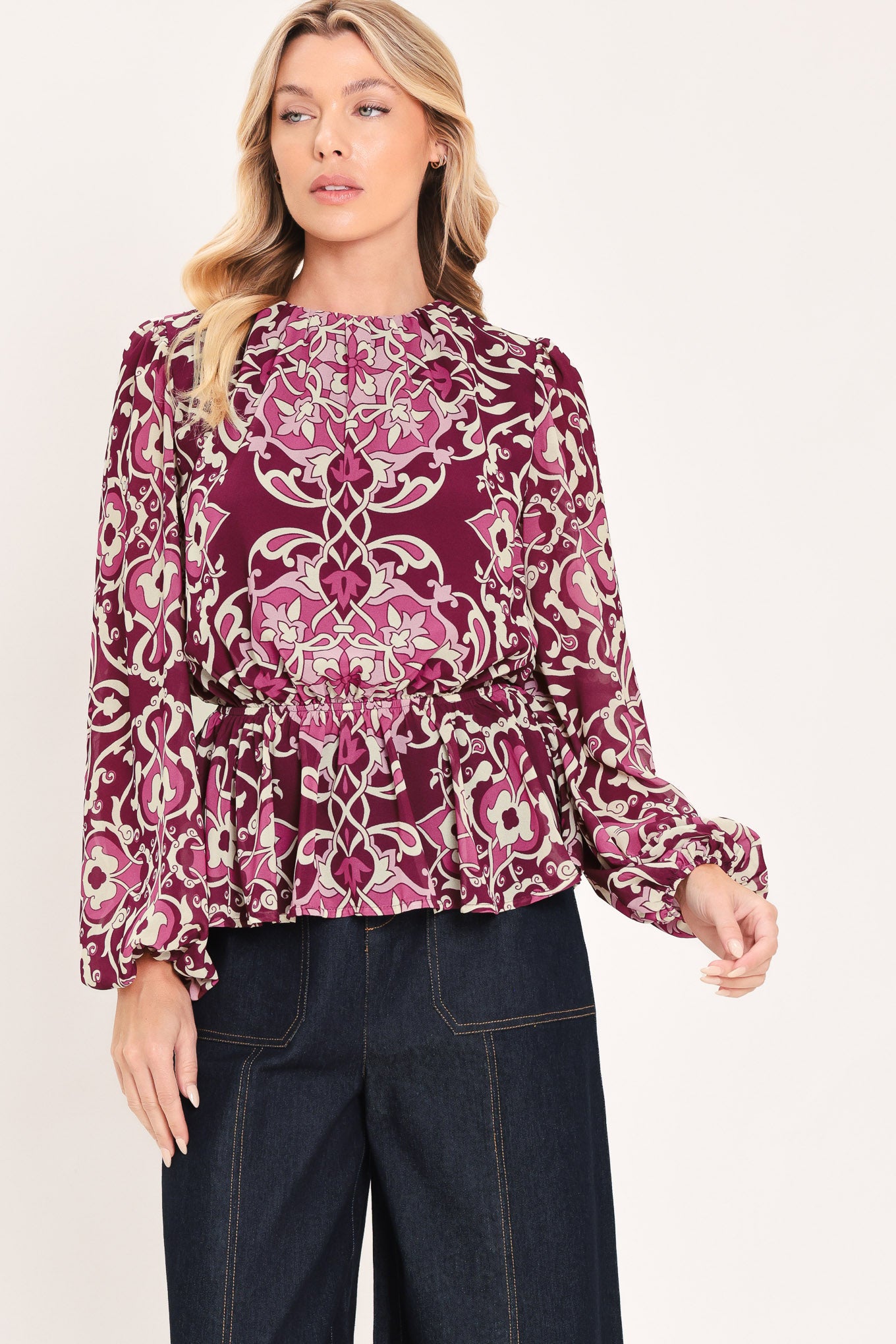 A woman modeling a long-sleeve peplum blouse with a burgundy and beige baroque-style pattern | Flying Tomato