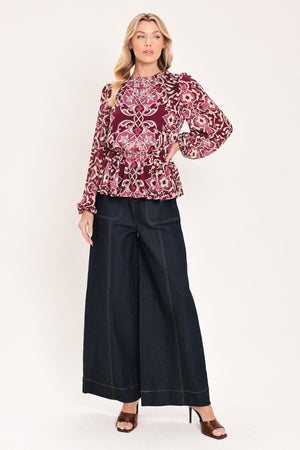 A woman modeling a long-sleeve peplum blouse with a burgundy and beige baroque-style pattern | Flying Tomato