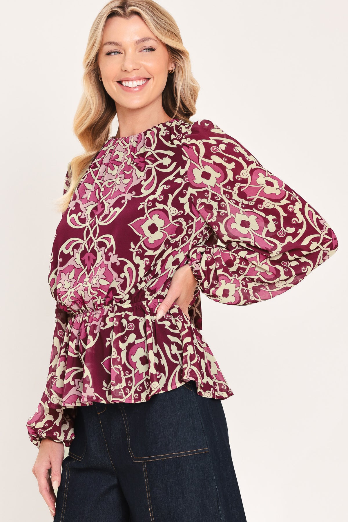 A woman modeling a long-sleeve peplum blouse with a burgundy and beige baroque-style pattern | Flying Tomato