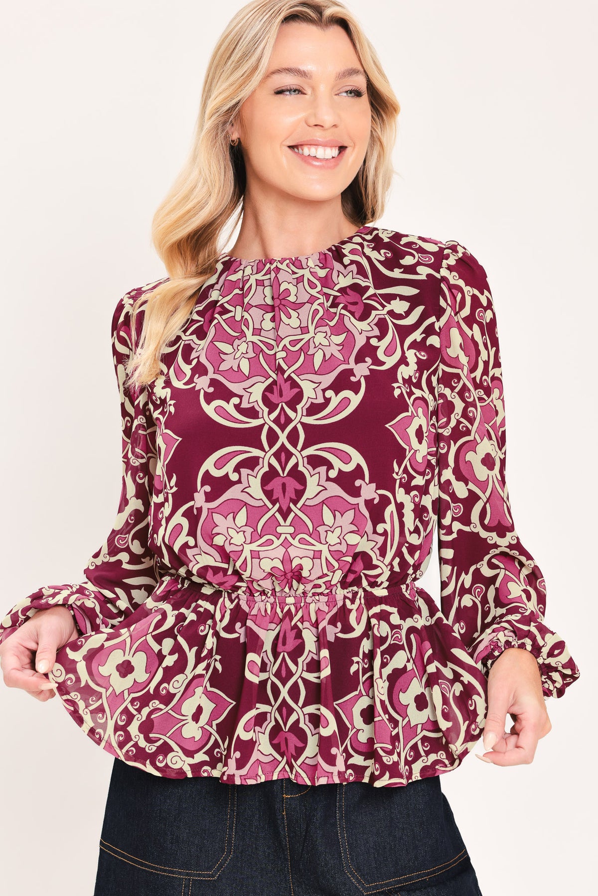 A woman modeling a long-sleeve peplum blouse with a burgundy and beige baroque-style pattern | Flying Tomato