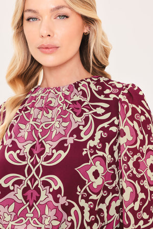 A woman modeling a long-sleeve peplum blouse with a burgundy and beige baroque-style pattern | Flying Tomato