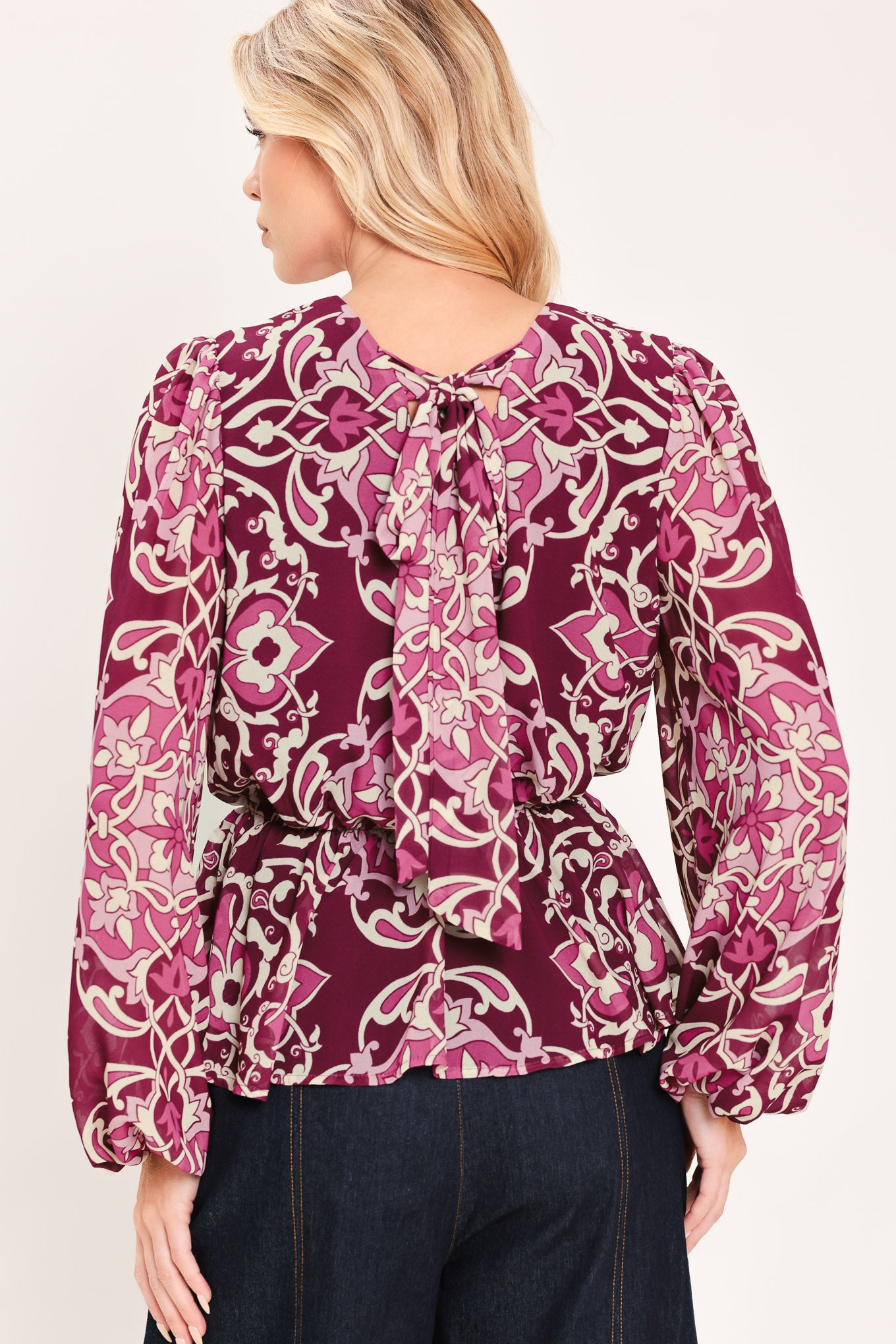A woman modeling a long-sleeve peplum blouse with a burgundy and beige baroque-style pattern | Flying Tomato