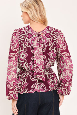A woman modeling a long-sleeve peplum blouse with a burgundy and beige baroque-style pattern | Flying Tomato