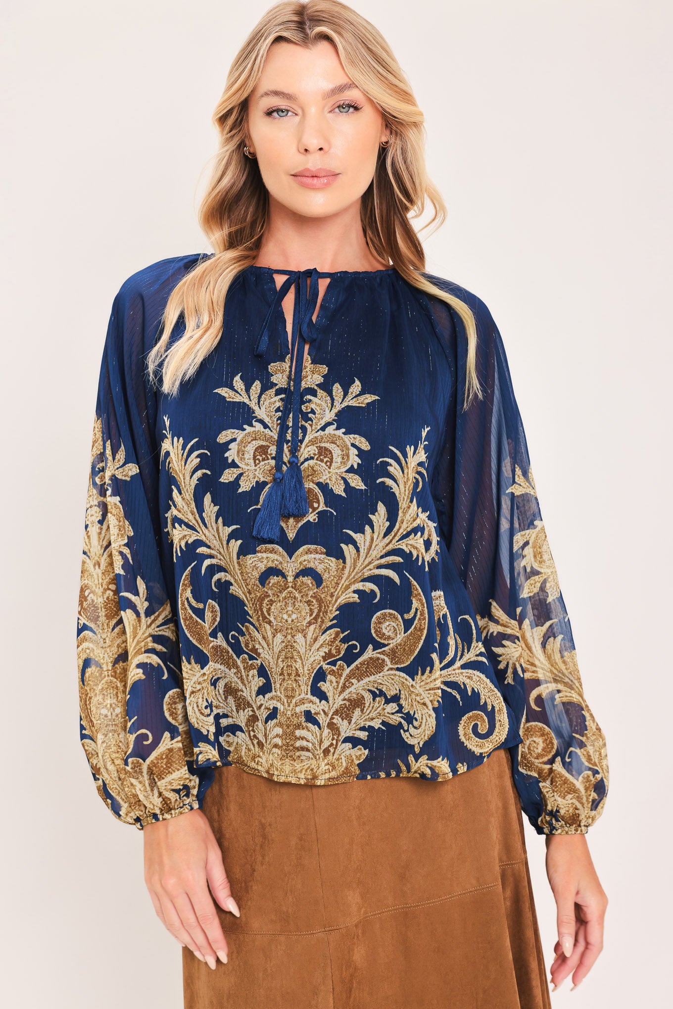 A woman wearing a navy blue long-sleeve blouse with an ornate gold baroque-style pattern and a tie-neck detail | Flying Tomato