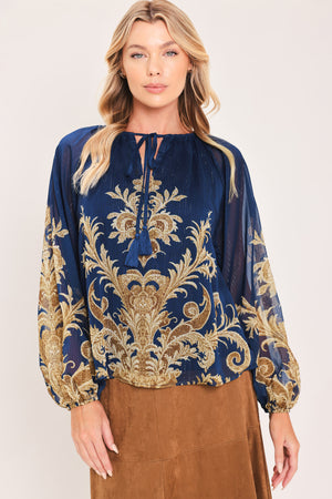 A woman wearing a navy blue long-sleeve blouse with an ornate gold baroque-style pattern and a tie-neck detail | Flying Tomato