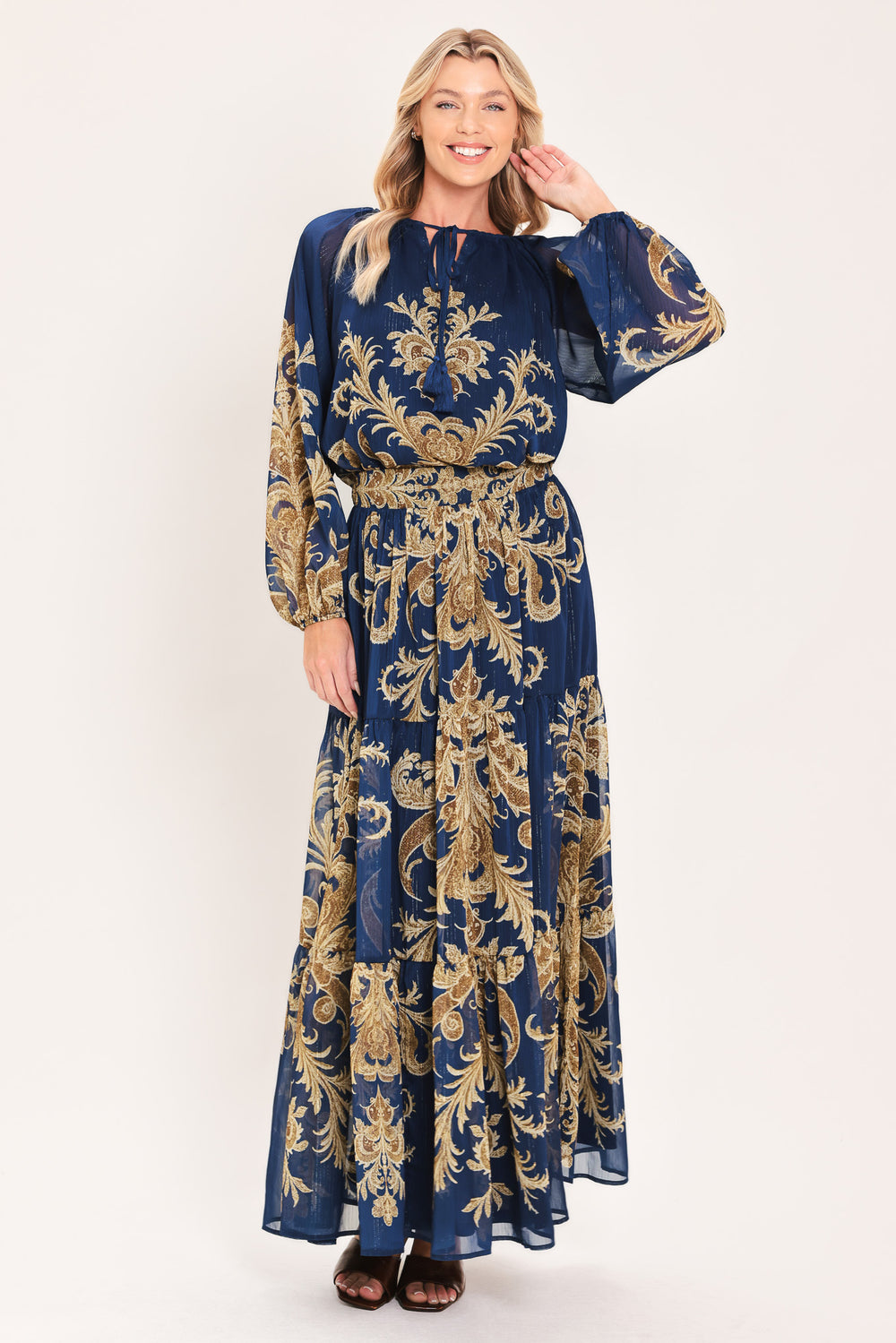 A woman wearing a navy blue long-sleeve blouse with an ornate gold baroque-style pattern and a tie-neck detail | Flying Tomato