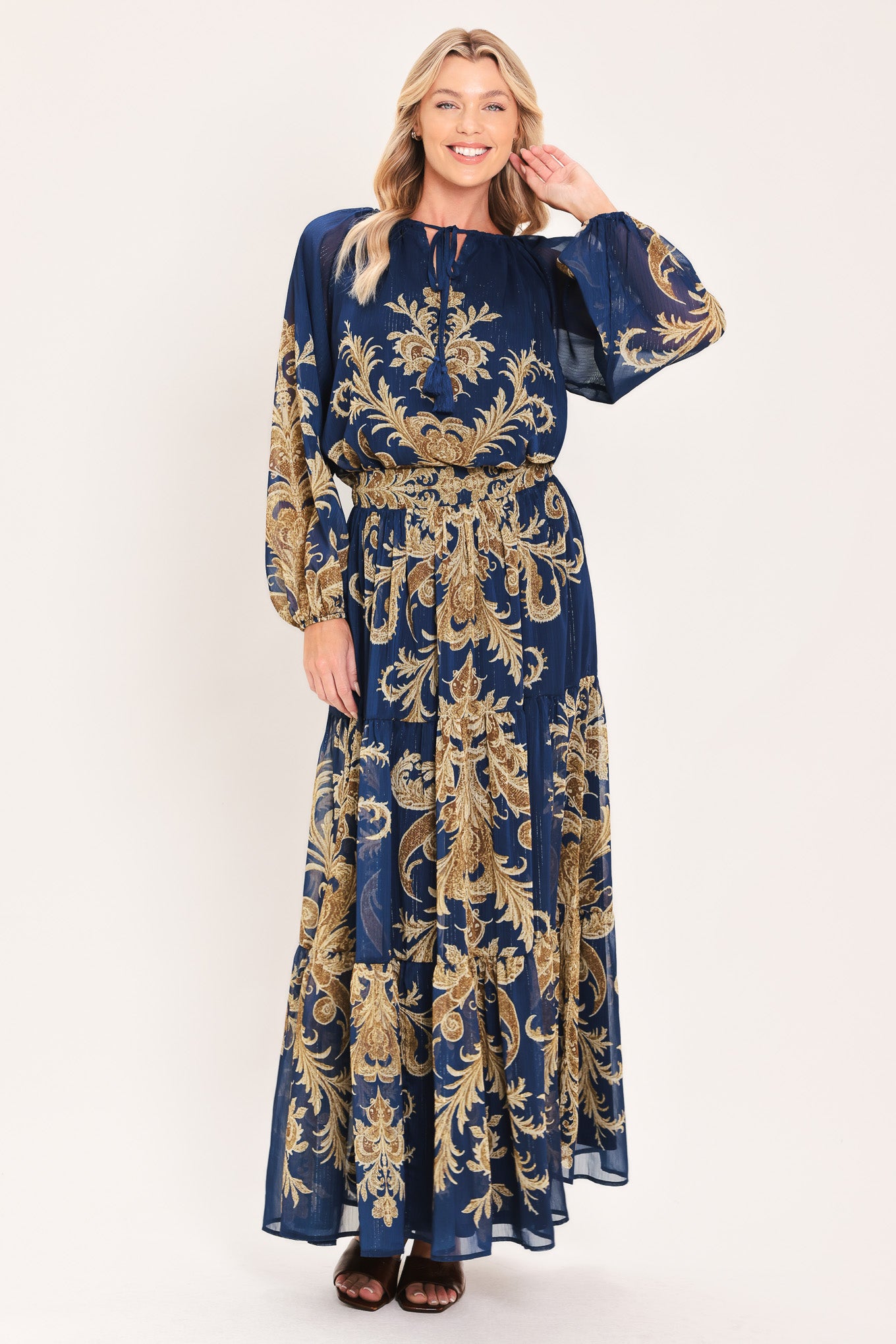 A woman wearing a navy blue long-sleeve blouse with an ornate gold baroque-style pattern and a tie-neck detail | Flying Tomato
