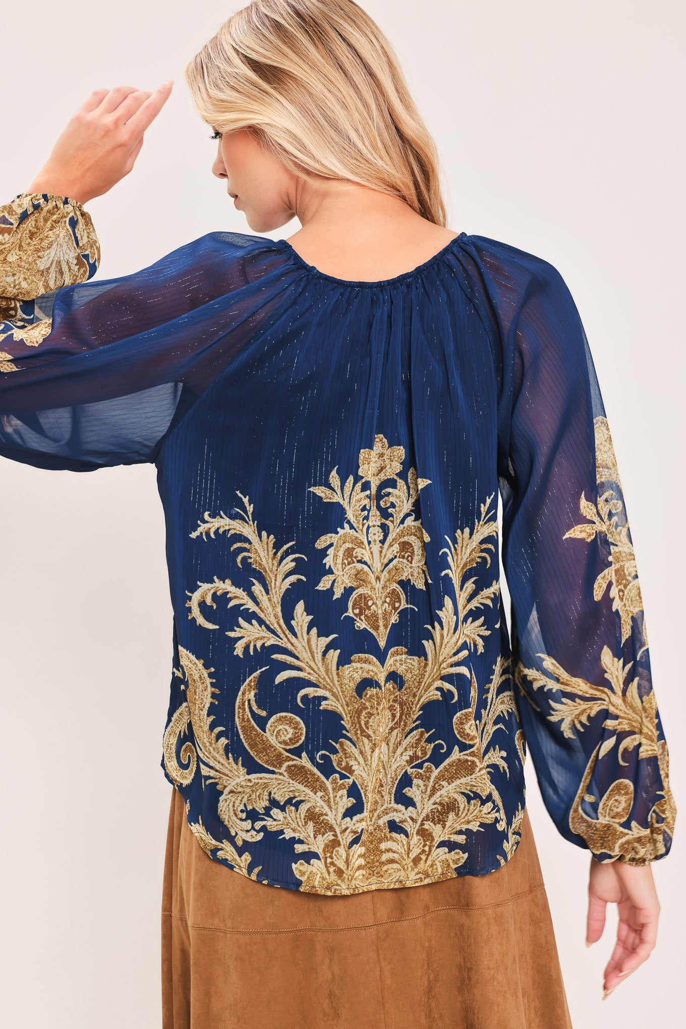 A woman wearing a navy blue long-sleeve blouse with an ornate gold baroque-style pattern and a tie-neck detail | Flying Tomato