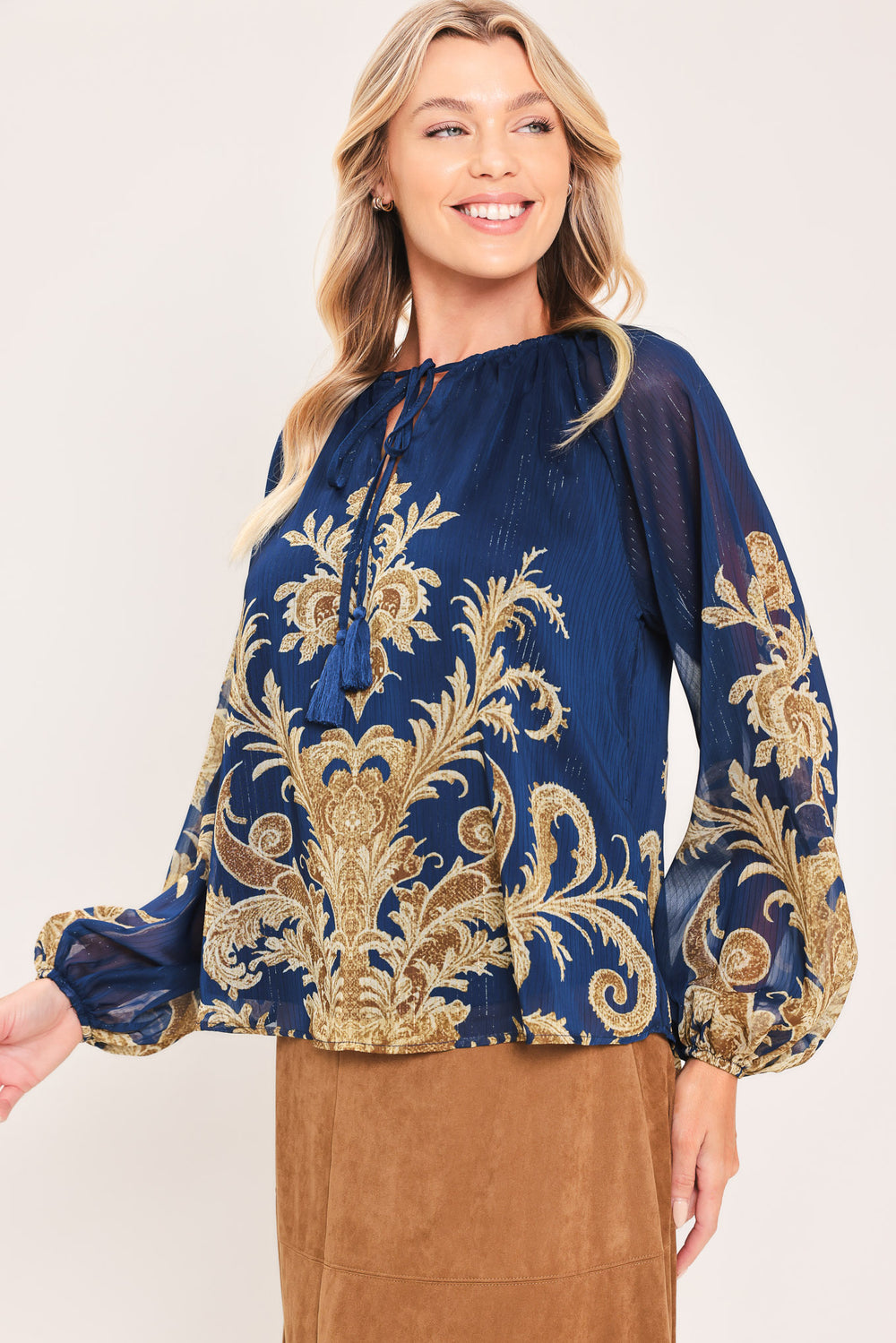 A woman wearing a navy blue long-sleeve blouse with an ornate gold baroque-style pattern and a tie-neck detail | Flying Tomato