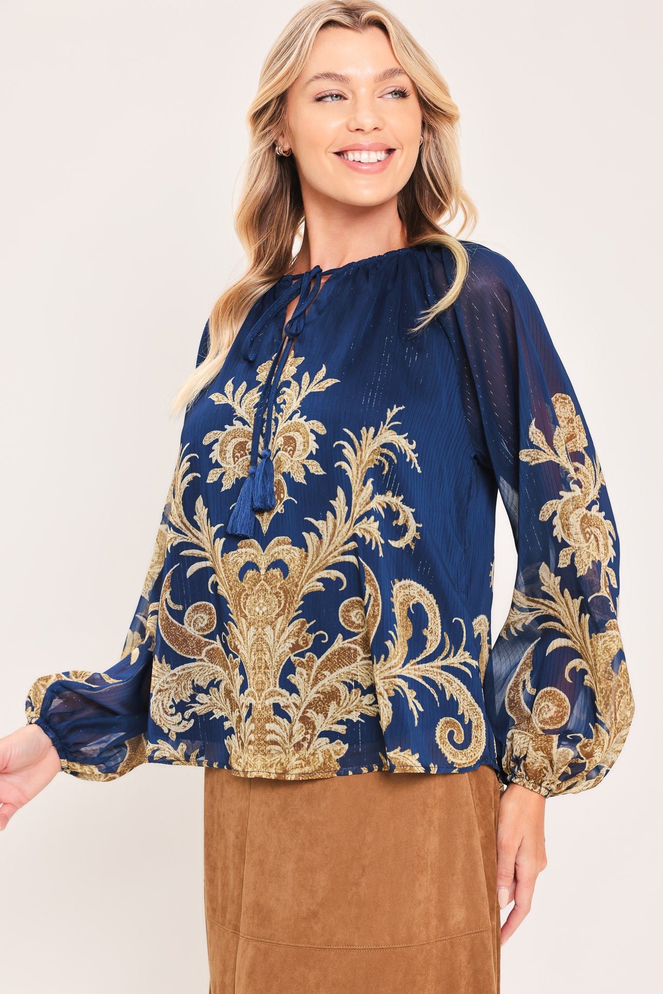 A woman wearing a navy blue long-sleeve blouse with an ornate gold baroque-style pattern and a tie-neck detail | Flying Tomato