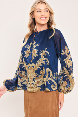 A woman wearing a navy blue long-sleeve blouse with an ornate gold baroque-style pattern and a tie-neck detail | Flying Tomato